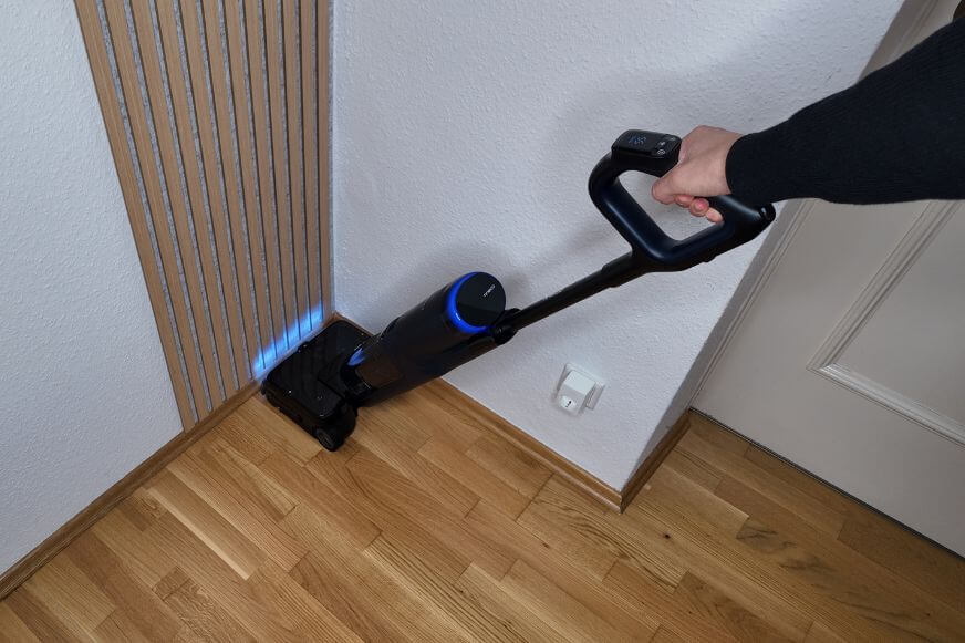 Tineco S7 Max Pro Laser beim Reinigen in einer Ecke macht versteckten Schmutz in dunkleren Bereichen sichtbar.